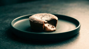Un fondant au chocolat au cœur coulant saupoudré de sucre glace sur une assiette sombre.