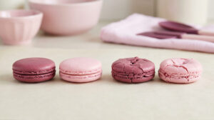 Quatre macarons roses sur du papier sulfurisé, deux réussis et deux fissurés.