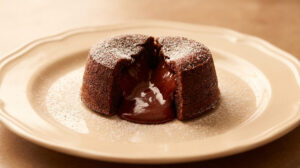 Un fondant au chocolat saupoudré de sucre glace sur une assiette, révélant un cœur fondant et chocolaté.