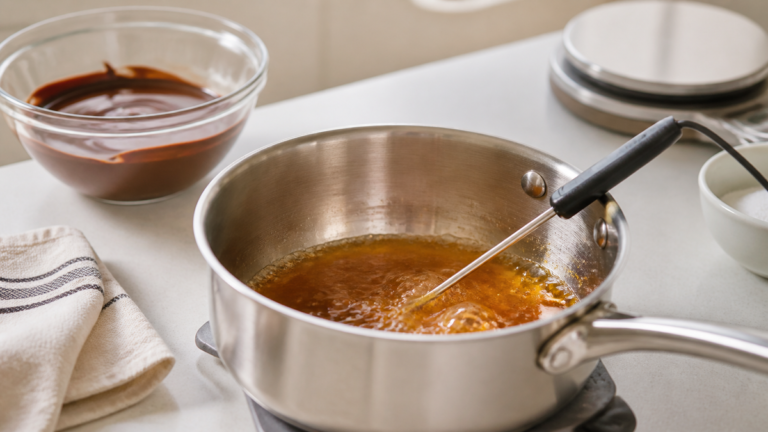 Sonde de cuisson plongeante dans une casserole de caramel doré sur un plan de travail de pâtisserie
